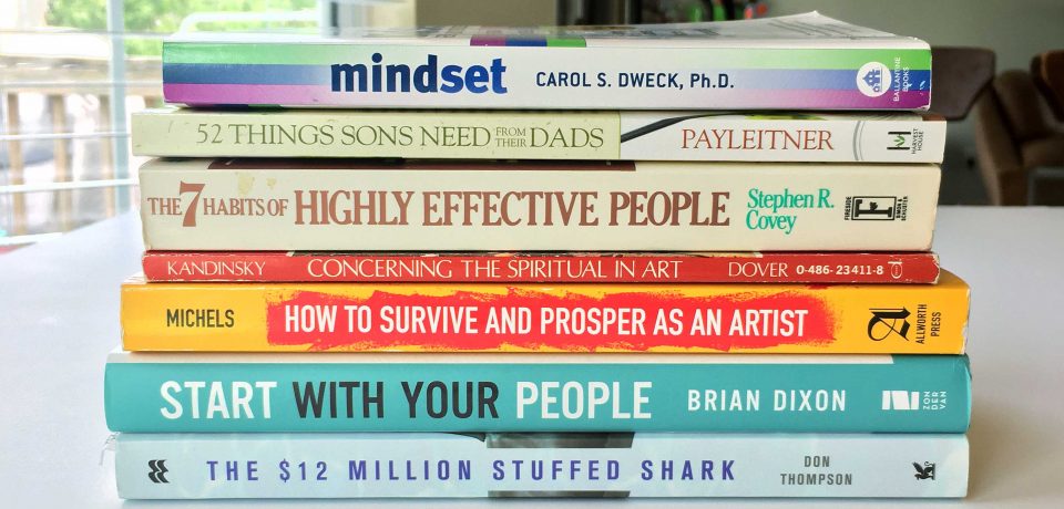 Brad Blackman's Reading Stack for Summer 2020 includes Mindset by Carol S. Dweck, 52 Things Sons Need from their Dads by Jay Payleitner, The 7 habits of Highly Effective People by Stephen R. Covey, Concerning the Spiritual in Art by Wassily Kandinsky, How to Survive and Prosper as an Artist (7th Edition) by Carroll Michels, Start with Your People by Brian Dixon, and The $12 Million Stuffed Shark by Don Thompson.